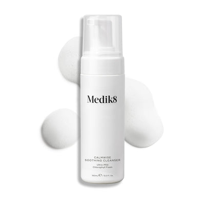 Medik8 Calmwise Soothing Cleanser pump bottle displayed on a white background with a smear of white foam behind it, highlighting the product's texture.