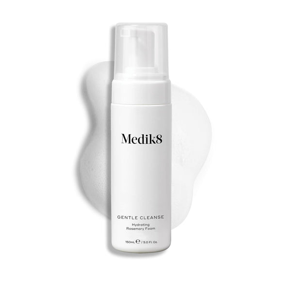 A Medik8 Gentle Cleanse pump bottle displayed on a white background with a smear of white foam behind it, highlighting the product's hydrating texture.-18