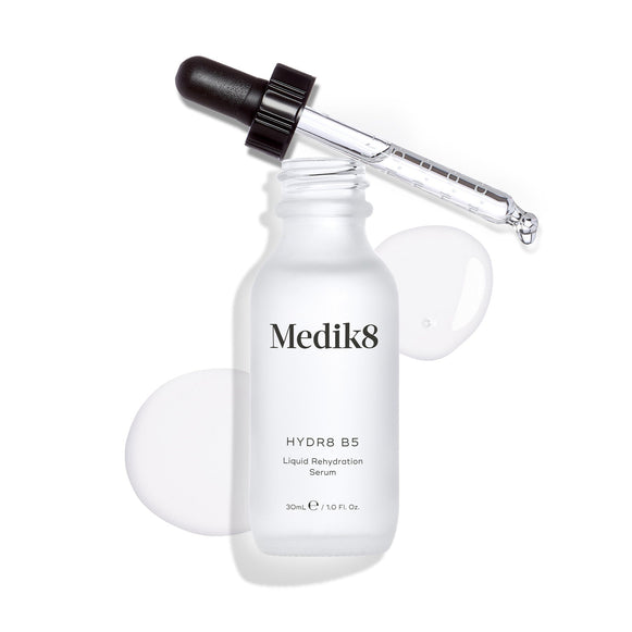 Medik8 Hydr8 B5 serum bottle stands against a clean white background with a clear liquid puddle and droplets, with the dropper resting on top. Text identifies the product as a 30mL  Liquid Rehydration Serum. -21