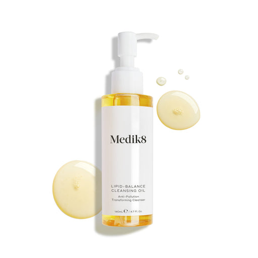 Medik8 Lipid-Balance Cleansing Oil bottle stands against a white background. Golden oil droplets surround the bottle, highlighting its rich, fluid texture.