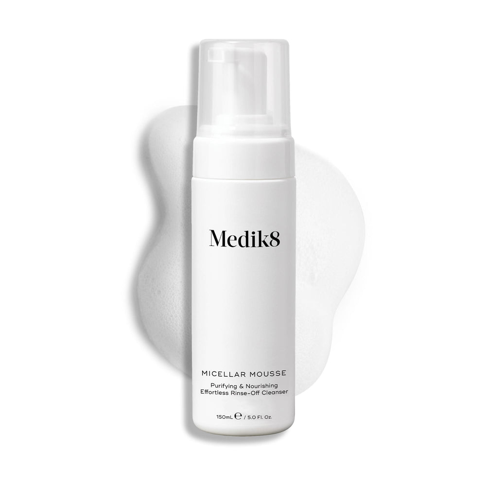 Medik8 Micellar Mousse pump bottle displayed on a white background with a smear of white foam behind it, highlighting the product's texture.