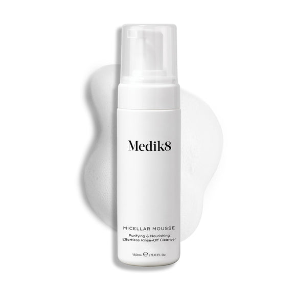 Medik8 Micellar Mousse pump bottle displayed on a white background with a smear of white foam behind it, highlighting the product's texture.-30