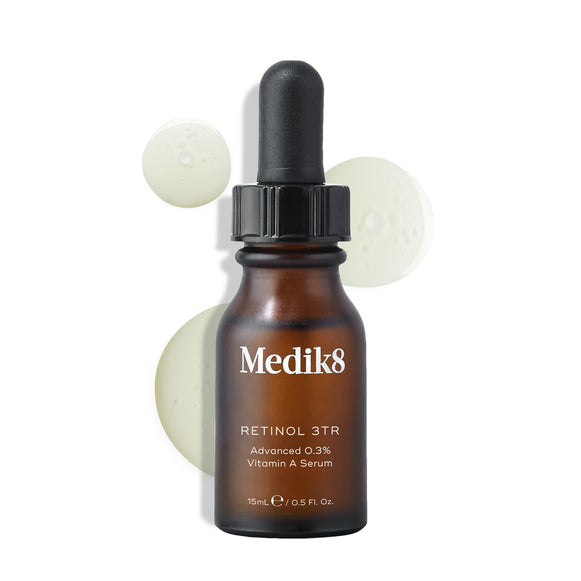 Medik8 Retinol 3TR serum bottle displayed against a clean white background with translucent serum droplets. The amber glass bottle with a black dropper cap features the Medik8 logo and is labeled  RETINOL 3TR Advanced 0.3% Vitamin A Serum  in a 15mL size.-23