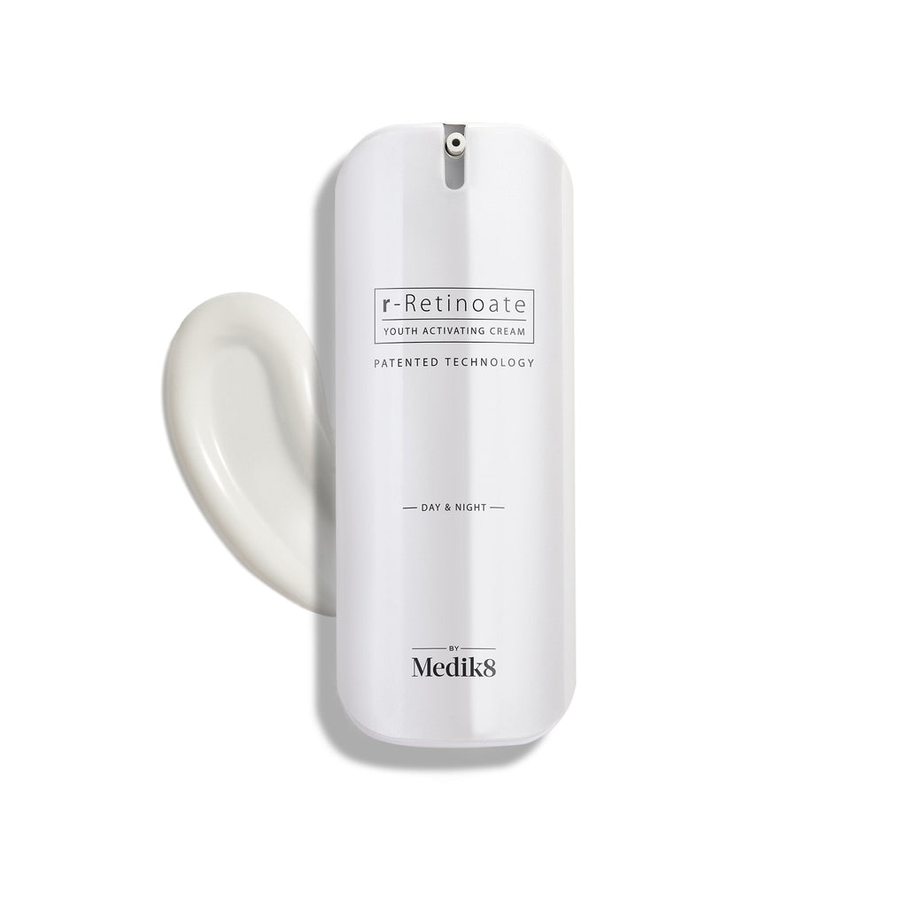 A sleek white pump bottle of r-Retinoate Day & Night stands upright, with a swirl of white cream next to it.