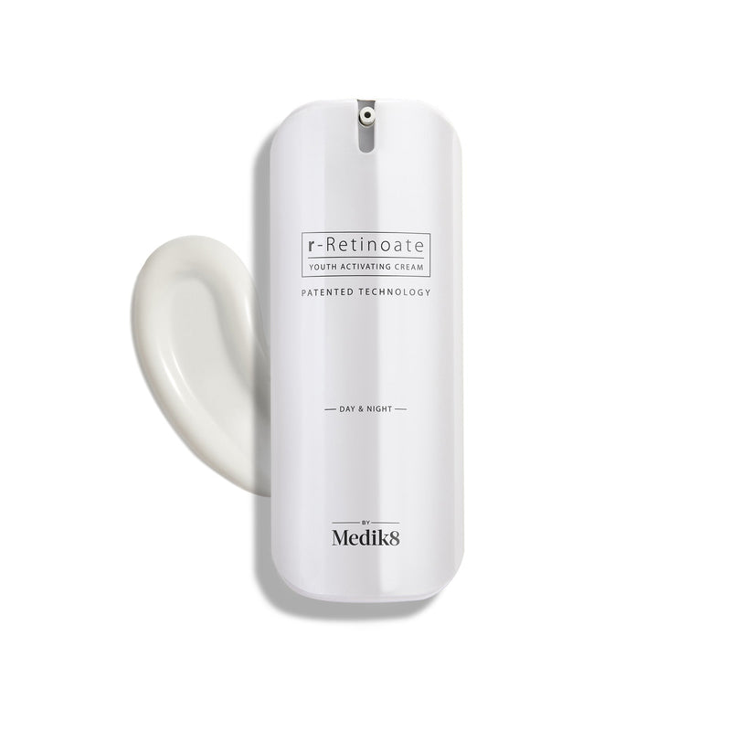 A sleek white pump bottle of r-Retinoate Day & Night stands upright, with a swirl of white cream next to it.