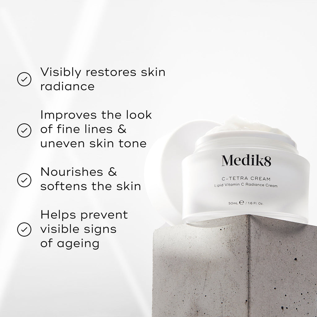 "Medik8 C-Tetra Cream jar displayed on a grey stone block against a white background with soft light rays. The image features four check-marked claims:

Visibly restores skin radiance

Improves the look of fine lines & uneven skin tone

Nourishes & softens the skin

Helps prevent visible signs of ageing"