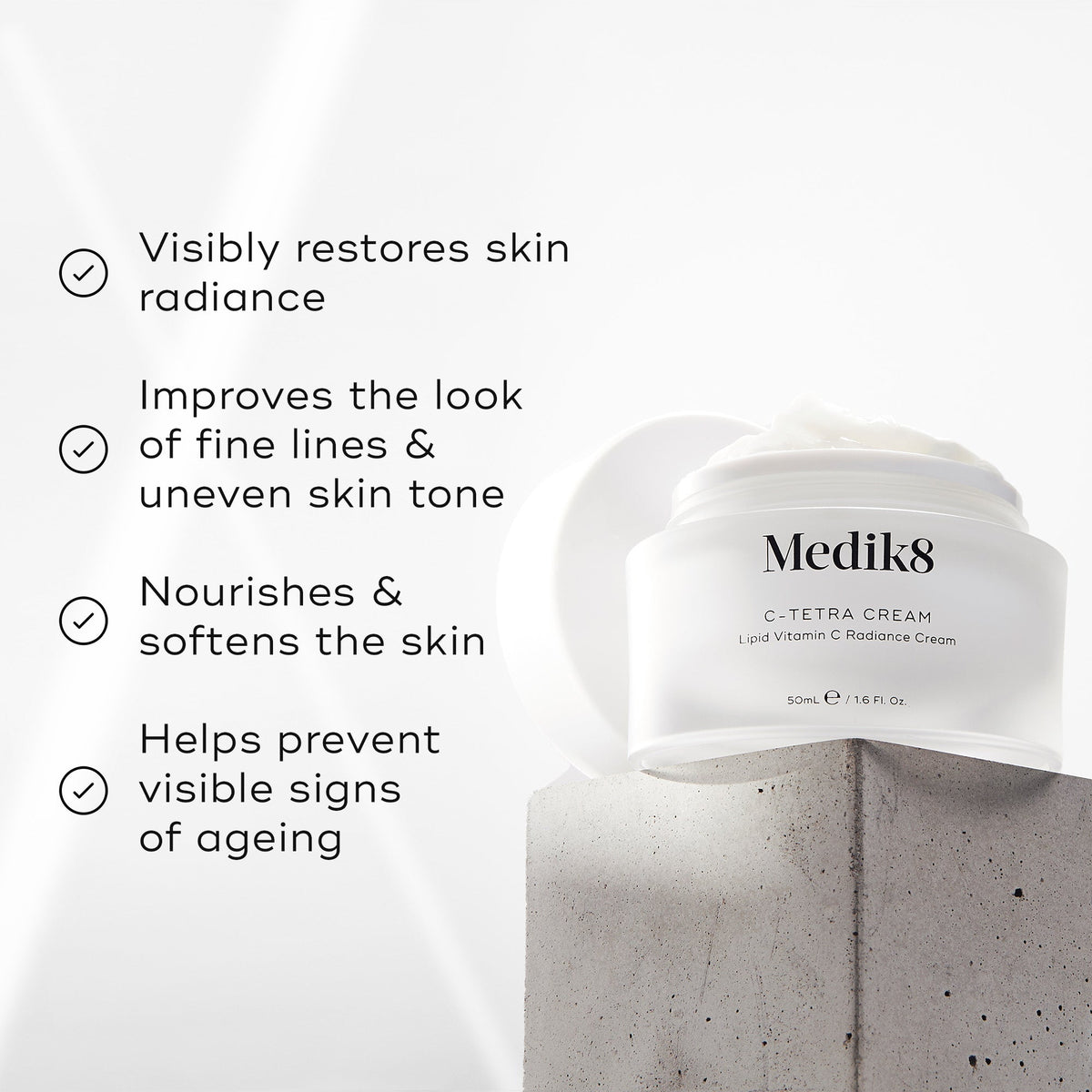 "Medik8 C-Tetra Cream jar displayed on a grey stone block against a white background with soft light rays. The image features four check-marked claims:

Visibly restores skin radiance

Improves the look of fine lines & uneven skin tone

Nourishes & softens the skin

Helps prevent visible signs of ageing"