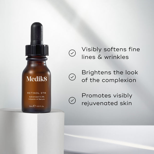 "Medik8 Retinol 3TR serum bottle stands on a white stone block against a clean white background with soft light rays. The image features three check-marked claims:

Visibly softens fine lines & wrinkles

Brightens the look of the complexion

Promotes visibly rejuvenated skin"