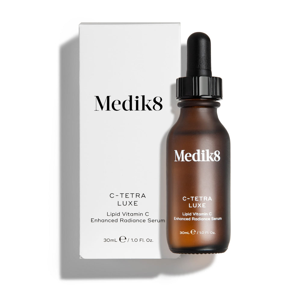 Medik8 C-Tetra Luxe serum bottle and its white cardboard carton displayed on a clean white background with soft shadows. The amber glass bottle and white box both feature the Medik8 logo and identify the product as  C-TETRA LUXE Lipid Vitamin C Enhanced Radiance Serum  in a 30mL size.