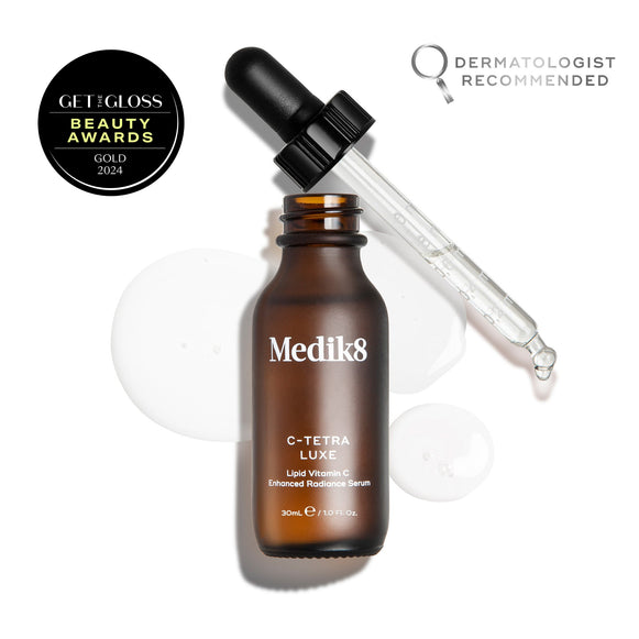 Medik8 C-Tetra Luxe serum bottle shown open with its glass pipette resting against the rim, displayed on a white background with clear, translucent serum droplets. The image includes a  GET THE GLOSS BEAUTY AWARDS GOLD 2024  seal in the top left and a  DERMATOLOGIST RECOMMENDED  emblem with a magnifying glass icon in the top right.-11