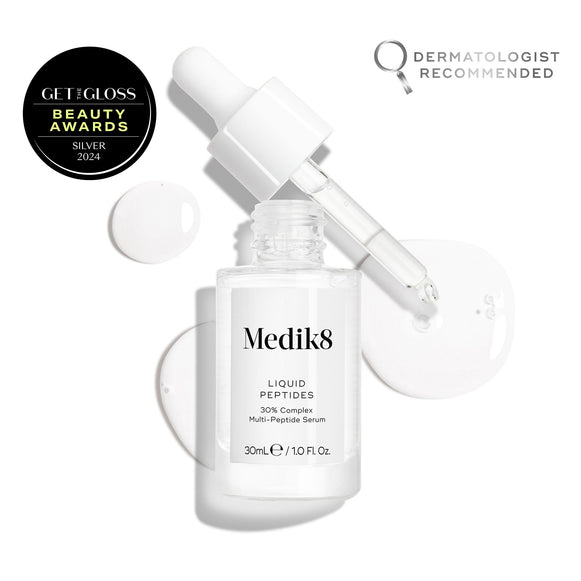 A clear glass dropper bottle of Liquid Peptides serum is presented, with its dropper removed and resting beside it and serum droplets, showing the texture-15