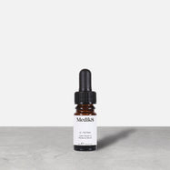 A travel-sized 8mL amber glass bottle of Medik8 C-Tetra lipid vitamin C radiance serum standing next to its white cardboard carton. The products are displayed on a textured grey surface against a clean white background