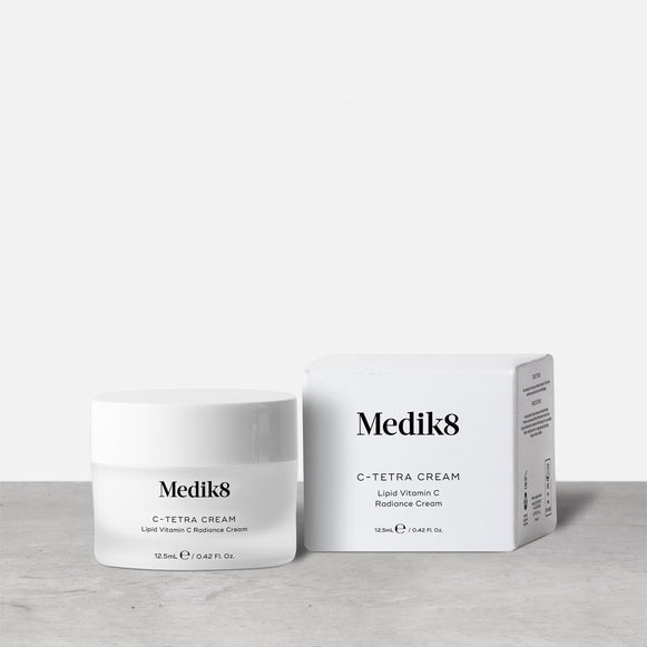 A 12.5ml white jar of Medik8 C-Tetra Cream, labeled "Lipid Vitamin C Radiance Cream," stands next to its corresponding white packaging box on a grey surface against a clean white background.-31