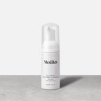 A travel-size pump bottle (40ml) of Medik8 Calmwise Soothing Cleanser displayed on a grey surface. Text describes it as an  Ultra-Mild Chlorophyll Foam. 