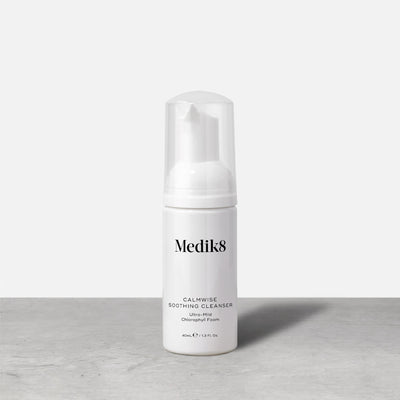 A travel-size pump bottle (40ml) of Medik8 Calmwise Soothing Cleanser displayed on a grey surface. Text describes it as an  Ultra-Mild Chlorophyll Foam. 