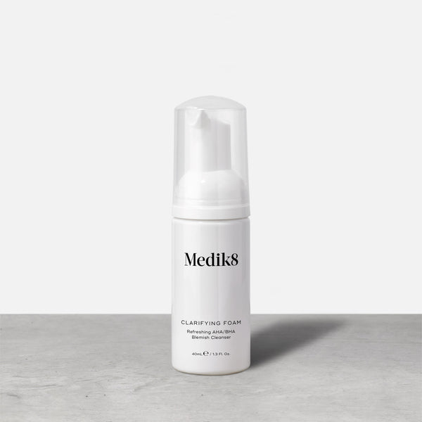 Bottle of Medik8 Clarifying Foam Refreshing AHA/BHA Blemish Cleanser stands against a grey and white background. The 40ml bottle has a clear cap and pump dispenser. 
