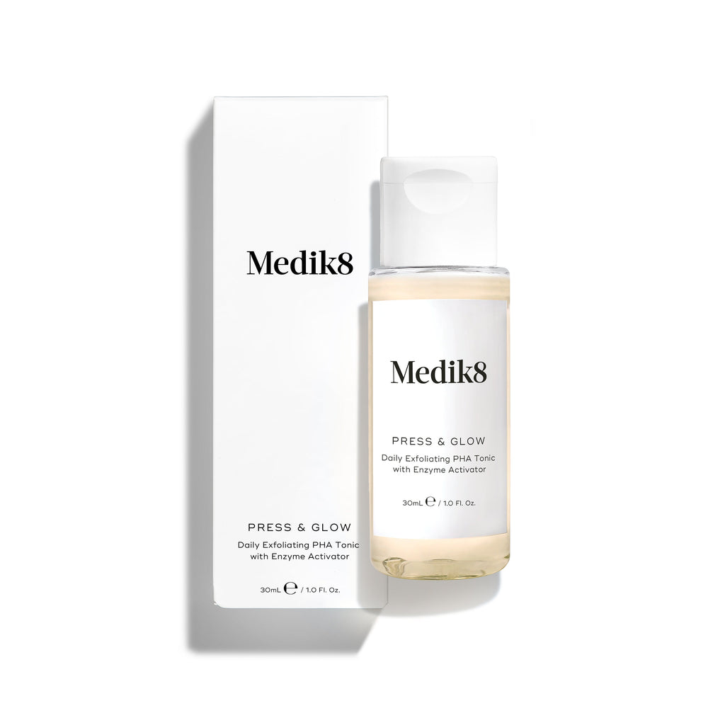 Medik8 Press & Glow tonic bottle stands in front of its matching white product carton on a clean white background. Text on both identifies the product as a travel sized Daily Exfoliating PHA Tonic with Enzyme Activator. 
