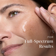 Close-up of a smiling woman touching her cheek where a dab of clear serum is applied. Text on the right reads  (For complete results).
