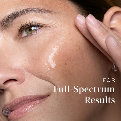 Close-up of a smiling woman touching her cheek where a dab of clear serum is applied. Text on the right reads  (For complete results).