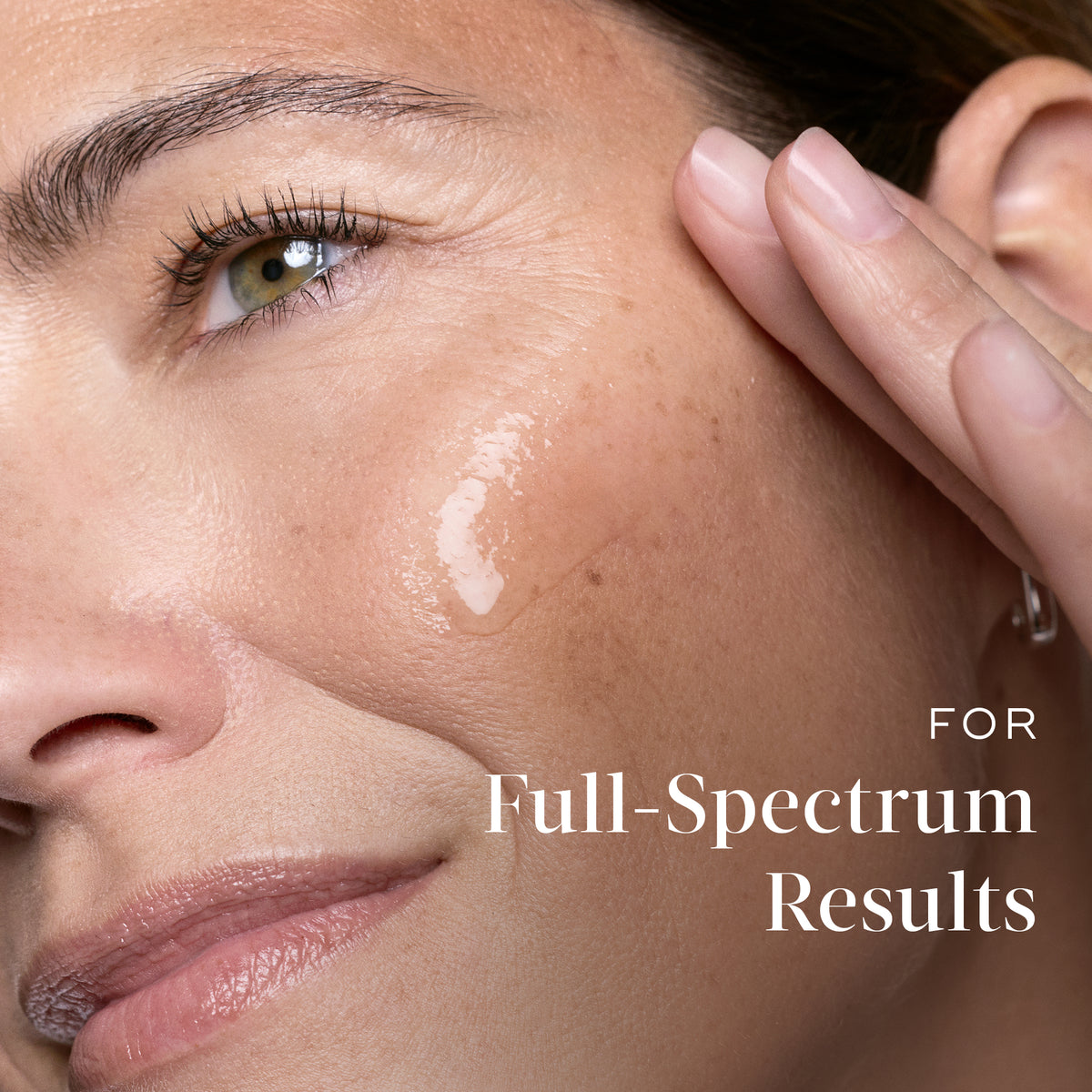 Close-up of a smiling woman touching her cheek where a dab of clear serum is applied. Text on the right reads  (For complete results).