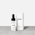 Medik8 Hydr8 B5 travel-sized serum bottle stands next to its matching white product carton on a grey textured surface against a neutral background. Text on the 8mL bottle identifies it as a "Liquid Rehydration Serum.