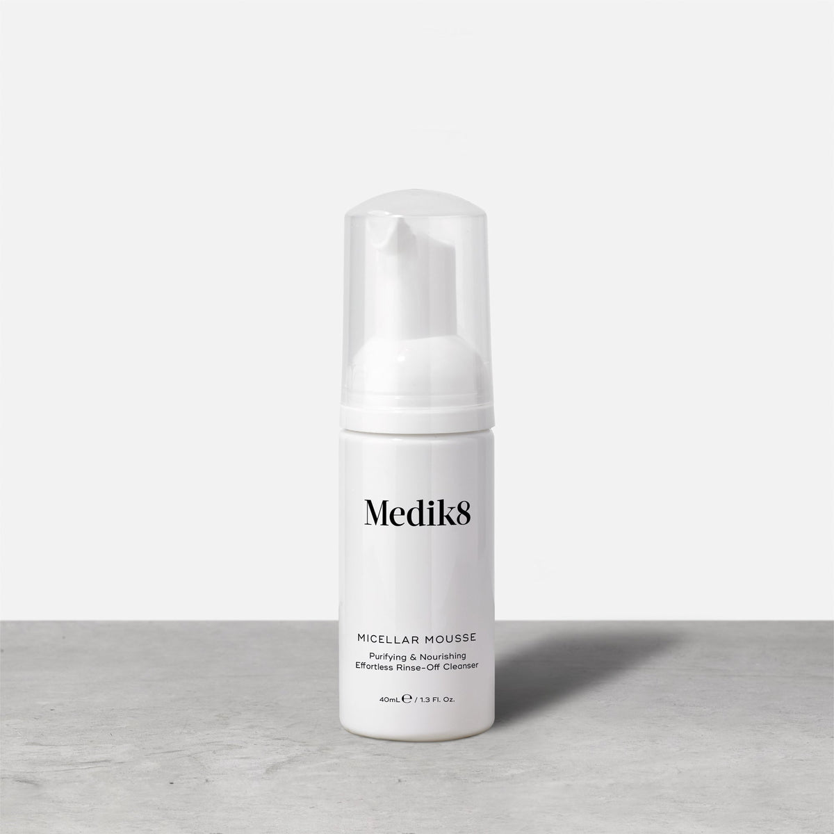 A travel-size pump bottle (40ml) of Medik8 Micellar Mousse displayed on a grey surface. Text describes it as a  Purifying & Nourishing Effortless Rinse-Off Cleanser. 