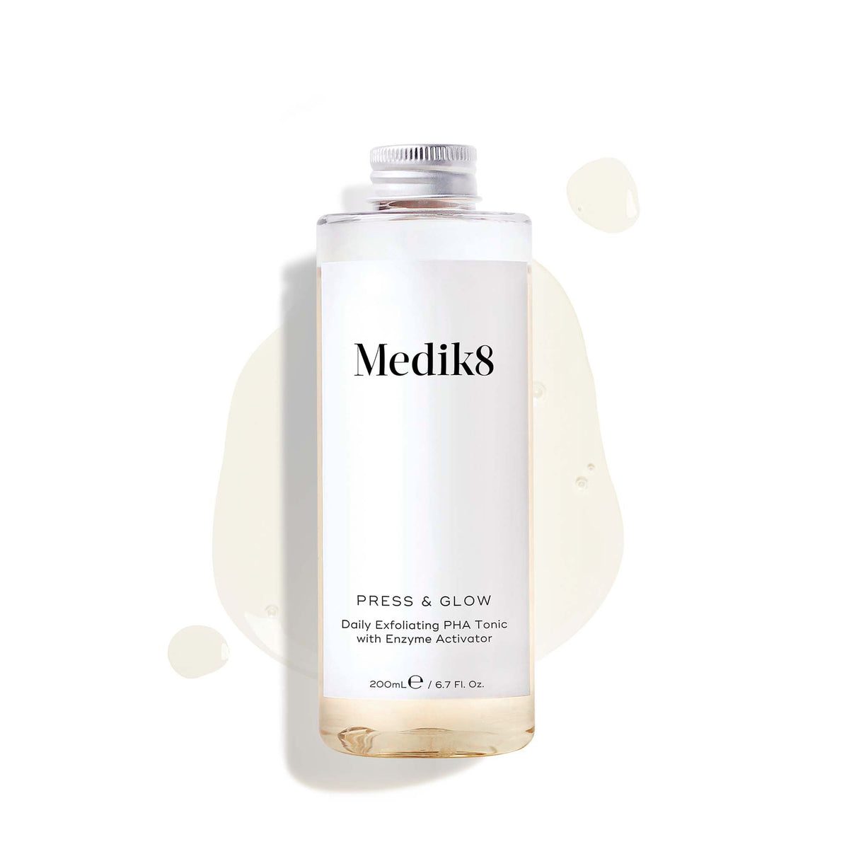 A 200mL clear refill bottle of Medik8 Press & Glow exfoliating tonic featuring a silver screw cap. Set against a white background, the bottle sits amidst a puddle and droplets of the pale yellow tonic, showcasing its liquid texture. The label text reads ""Daily Exfoliating PHA Tonic with Enzyme Activator."""