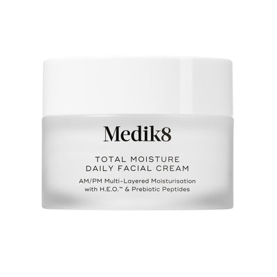 A travel-sized 12.5mL frosted jar of Medik8 Total Moisture Daily Facial Cream standing next to its white cardboard carton. The products are displayed on a textured grey surface against a clean white background. Text on both reads: "AM/PM Multi-Layered Moisturisation with H.E.O.™ & Prebiotic Peptides."