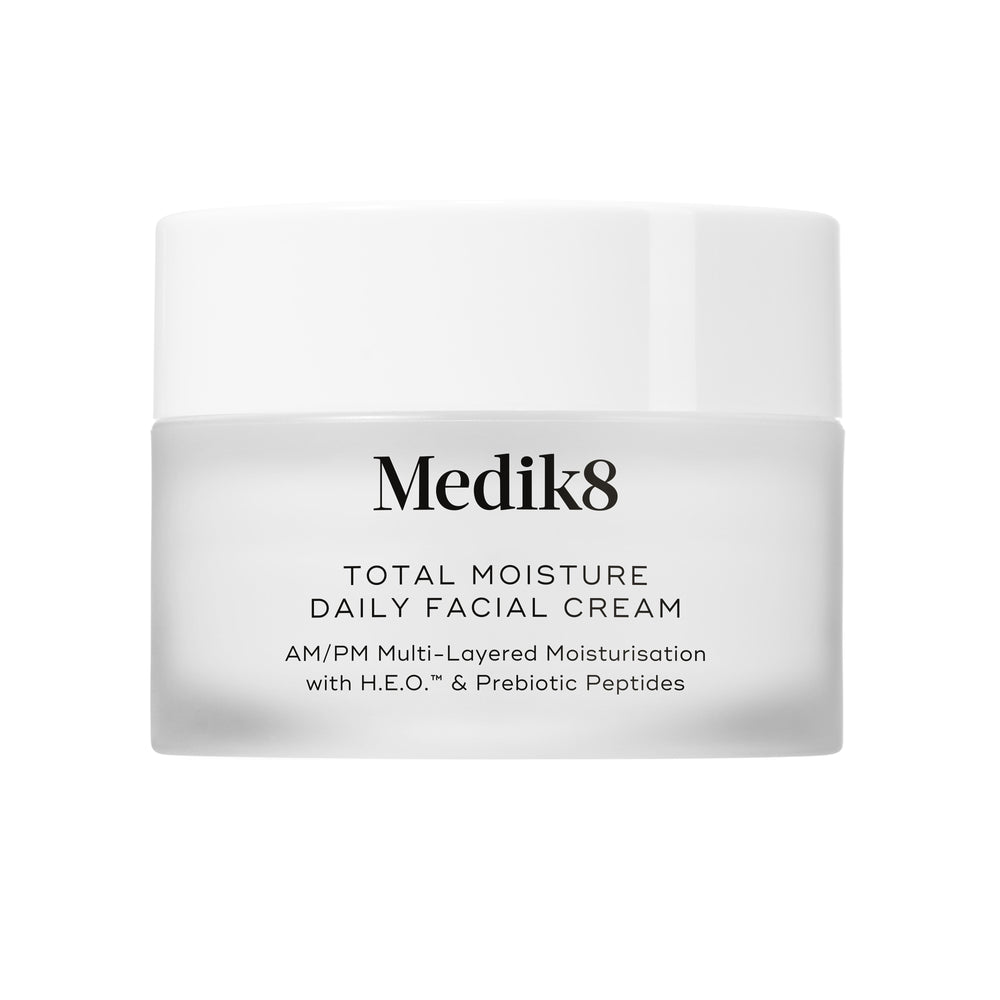 A travel-sized 12.5mL frosted jar of Medik8 Total Moisture Daily Facial Cream standing next to its white cardboard carton. The products are displayed on a textured grey surface against a clean white background. Text on both reads: "AM/PM Multi-Layered Moisturisation with H.E.O.™ & Prebiotic Peptides."