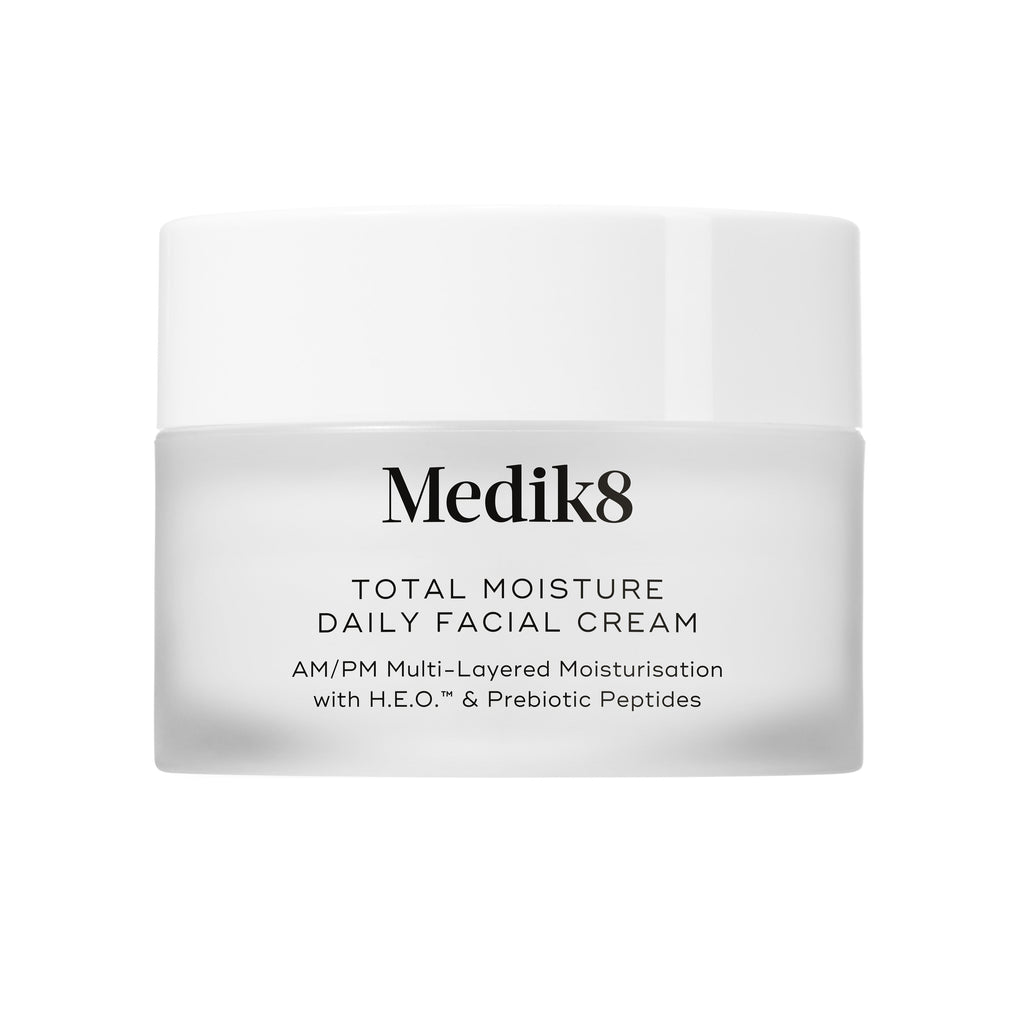 A travel-sized 12.5mL frosted jar of Medik8 Total Moisture Daily Facial Cream standing next to its white cardboard carton. The products are displayed on a textured grey surface against a clean white background. Text on both reads: "AM/PM Multi-Layered Moisturisation with H.E.O.™ & Prebiotic Peptides."